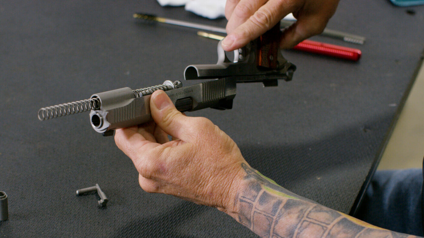 This image shows the meticulous cleaning process of the 1911 pistol’s slide after disassembly. The slide is being scrubbed with specialized cleaning brushes and solvent to remove carbon buildup and residue. Detailed textures on the metal surface and carefully arranged cleaning supplies emphasize thorough firearm maintenance. The picture demonstrates the combination of disassembly expertise and precise cleaning techniques. It is a step-by-step visual guide for ensuring the longevity and reliability of a 1911 pistol.